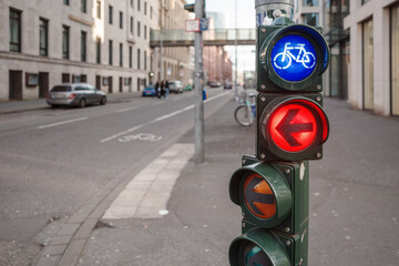 A close-up view of a traffic signal post at an urban intersection, showing a blue bicycle lane...