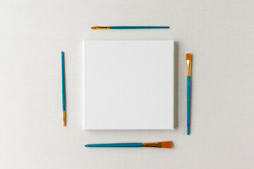 Blank white canvas surrounded by paint brushes - flat lay mockup