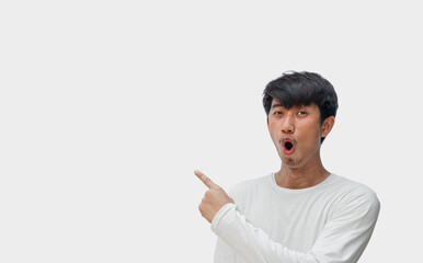 A young Asian man in his 20s wearing a white t-shirt happy shocked face pointing thumbs up isolated...