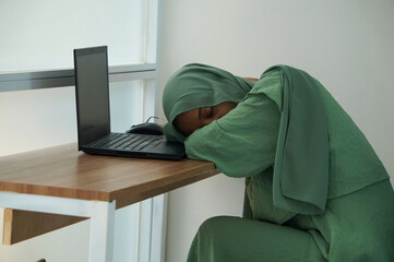 A muslim woman who is tired and asleep while working at home using a laptop