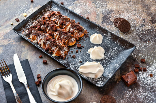 Oreo and Brownie Poffers with chocolate, whipped cream, knife and fork served in dish isolated on dark background closeup top view of cafe baked dessert food