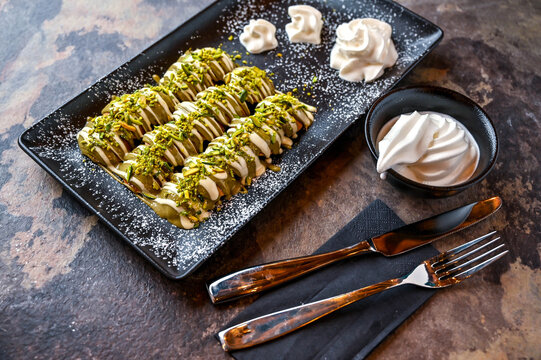 Pistachio Poffers with white chocolate, whipped cream, knife and fork served in dish isolated on dark background closeup top view of cafe baked dessert food