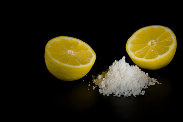 lemon cut in half with a pile of salt isolated on black background and copy space