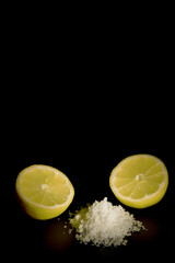 lemon cut in half with a pile of salt isolated on black background and copy space