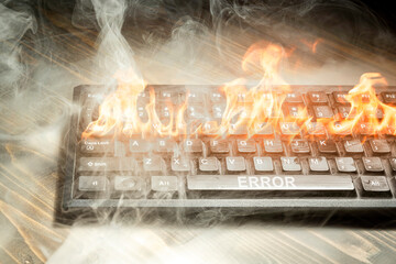 Computer keyboard burned with flame and smokes on wooden desk.