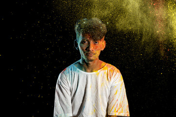 Asian man splashed with colorful holi powder and having fun isolated on black background.