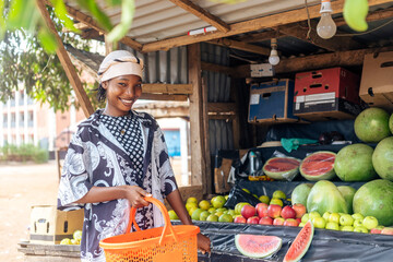 smiling woman holding shopping basket standing beside a farmers fruit shop