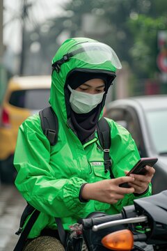 Indonesian woman holding cellphone accepting orders working as online motorcycle drivers in green safety driving clothing