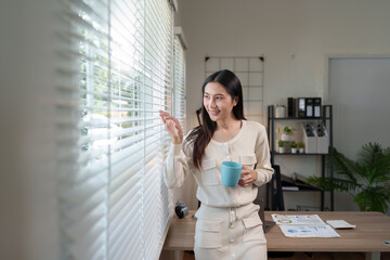 Fototapeta premium Confident Asian businesswoman working on real estate projects Online financial business, accounting, and drinking coffee while working, sitting happily in the office at home.