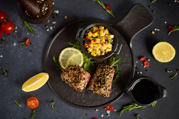 pieces of Organic grilled Tuna fillet covered with sesame seeds and mango salsa on black ceramic serving board