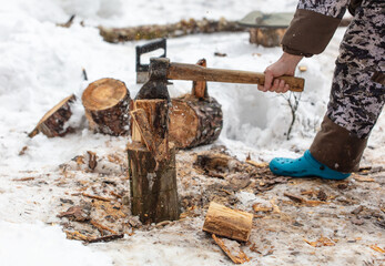 A man chops wood with an ax in the snow in winter
