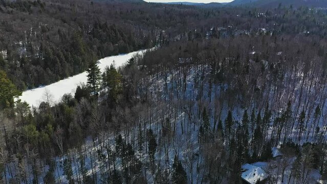 High aerial drone view of a country landscape in winter, showing lakes, mountains and trees with a cross country skiing trail in the woods of the Laurentians