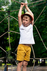 A child climbs up an alpine grid in a park on a playground on a hot summer day