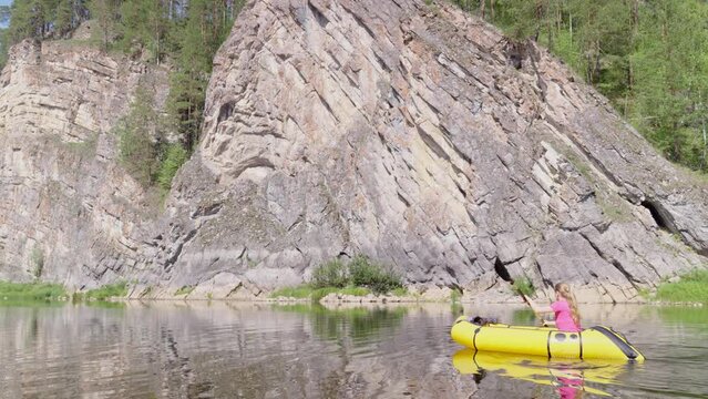 Woman traveler swims in boat on mountain river surrounded by high mountains. Girl kayak rafting rowing leisurely paddle along calm river. Packrafting