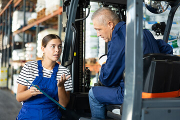 Young woman and elderly man working on loader in warehouse check documents © JackF