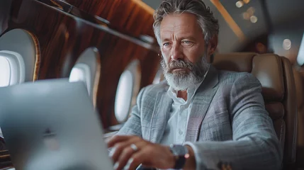 Papier Peint photo Ancien avion A middle aged businessman in suit working on laptop in plane during business trip.