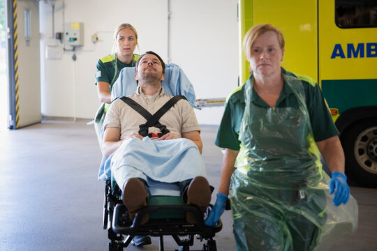Female rescue workers pulling male patient on gurney for emergency treatment in hospital