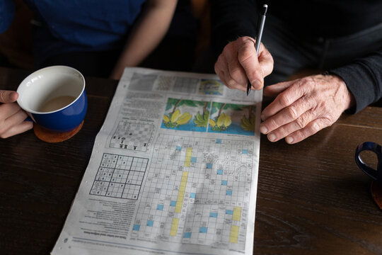 Midsection of elderly man solving crossword puzzle by caregiver on table at home