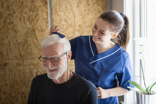 Happy female caregiver combing hair of senior man at home