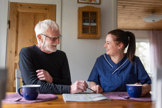 Happy senior man talking with female healthcare worker while solving sudoku at home