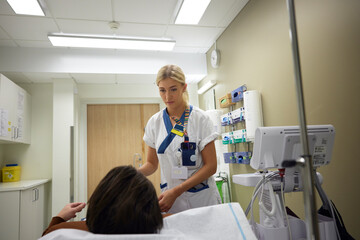Mid adult female doctor talking with male patient lying on bed in examination room