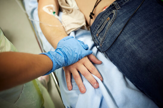 Midsection of female doctor touching male patient's hand lying on bed in hospital