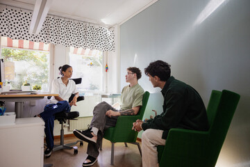 Teenage boys discussing problems with female counselor during group therapy in office