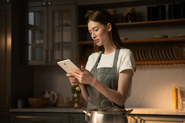 A focused young woman, clad in a casual apron, stands in a well-lit, contemporary kitchen. She is...