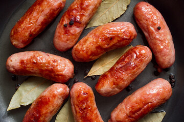 Fried meat sausages in a frying pan with spices. Lots of sausages. Top view.