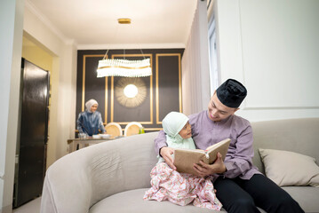 Portrait of Muslim father with his daughter holding koran while his wife preparing food for iftar on the dining table