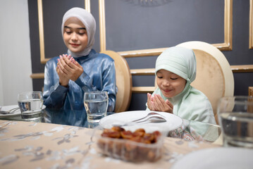Indonesian muslim family praying together for breakfasting with meals on the dining table during ramadan.