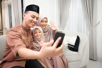 Young Indonesian family doing video call to other family and relatives with greetings gesture to...