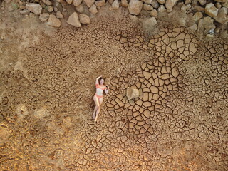 Aerial portrait of beautiful young lady in bikini lying on dry cracked red soil. arid, cracked red soil drought and arid climate conditions. Climate and weather change.