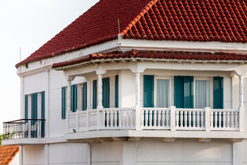 balcony of a beautiful old white house with green windows and a roof with a orange roof