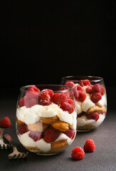 Italian dessert tiramisu with raspberries in a glass on a dark concrete background