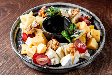 Various types of cheese, including sliced yellow and white cheeses, are neatly arranged. Red grapes add a pop of color, while walnuts provide texture. Fresh green mint leaves serve as a garnish