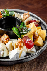 Various types of cheese, including sliced yellow and white cheeses, are neatly arranged. Red grapes add a pop of color, while walnuts provide texture. Fresh green mint leaves serve as a garnish