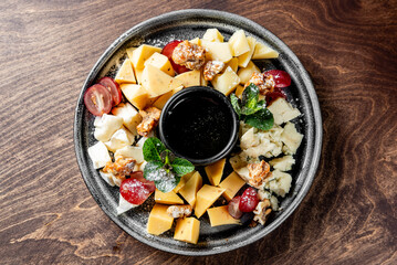 Various types of cheese, including sliced yellow and white cheeses, are neatly arranged. Red grapes add a pop of color, while walnuts provide texture. Fresh green mint leaves serve as a garnish
