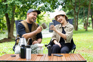 Happy asian couple clinking coffee mug together at camp side, They feeling relaxed and refreshing...