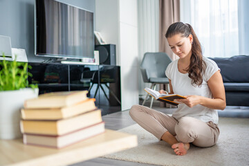 Young woman reading book and stack of books in the foreground