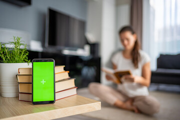 Digital detox concept photo. Smartphone with green chroma key screen and woman reading book in the...