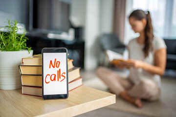 Digital detox concept photo. Smartphone with the text No Calls and woman reading book in the background - obrazy, fototapety, plakaty