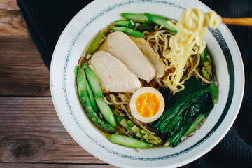 A bowl of noodles with chicken, asparagus, and egg