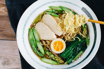 A bowl of ramen with chicken, asparagus, and egg