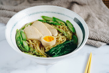 A bowl of ramen with chicken, asparagus, and egg