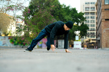 Shot of young male hip hop dancer in stylish clothes in motion dances in city street