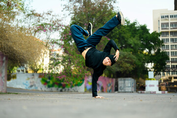 Shot of young male hip hop dancer in stylish clothes performing a handstand in city street