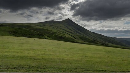 Fototapeta premium Grassy field near a grassy mountain under a cloudy sky