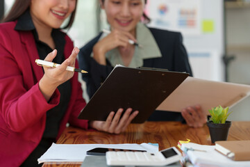 Two Asian businesswomen are brainstorming to analyze the financial reporting situation. Calculate investments, income, taxes, and accounting from the income graph data at your desk.