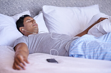 Man, music and cellphone in bed to relax, tired and audio podcast or audiobook for peace on weekend. Calm person, dream and rest on mobile for online meditation, happy and listening to radio in home